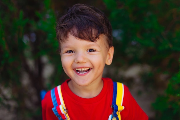 Un bambino felice guarda nella telecamera il ritratto luminoso e colorato di un ragazzo coraggioso con una maglietta rossa su un...