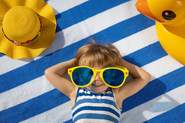 Happy child lying on striped towel outdoor. Top view portrait of kid. Funny baby smiling. Summer vacation concept