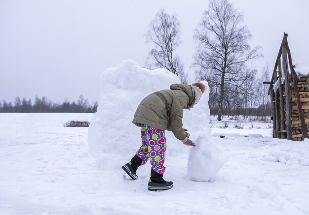 Happy child make a snowman in a snow-covered field in the countryside.