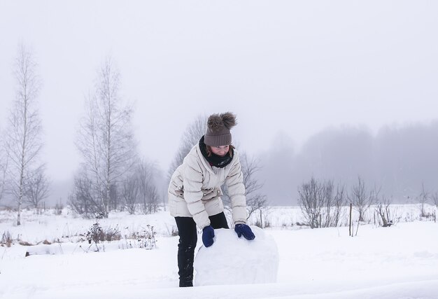 幸せな子供は田舎の雪に覆われたフィールドで雪だるまを作ります。