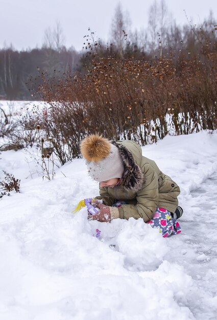 Счастливый ребенок делает снеговика на заснеженном поле в сельской местности