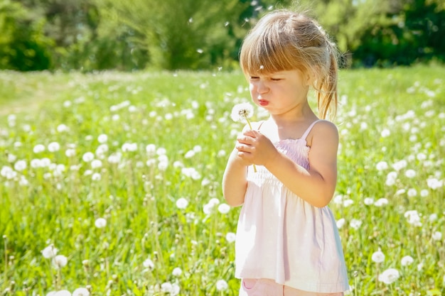 Happy child outdoors blowing dandelion in the park