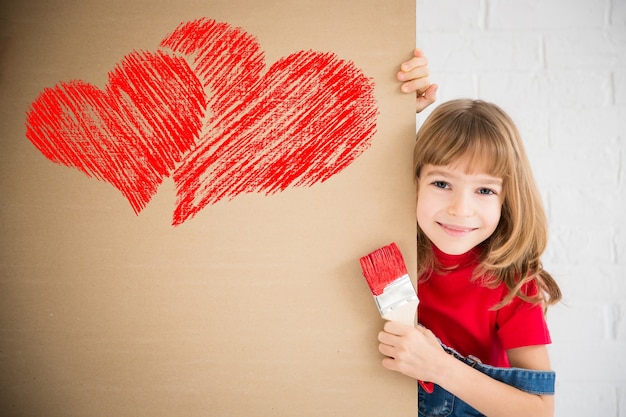 벽에 큰 붉은 마음을 그림 행복 한 아이. 집에서 놀고 재미있는 소녀. 발렌타인 데이 카드. 혁신 및 디자인 컨셉
