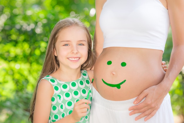 happy child painting smile on belly of pregnant woman family having fun outdoors in spring park