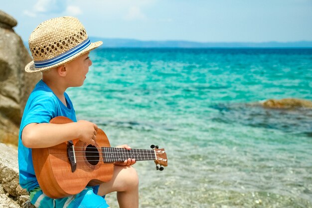 Bambino felice che gioca chitarra in riva al mare in grecia sullo sfondo della natura