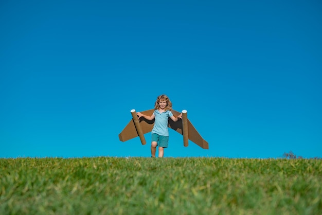 Photo happy child playing in park kid having fun with toy paper wings little boy in dreaming of becoming a