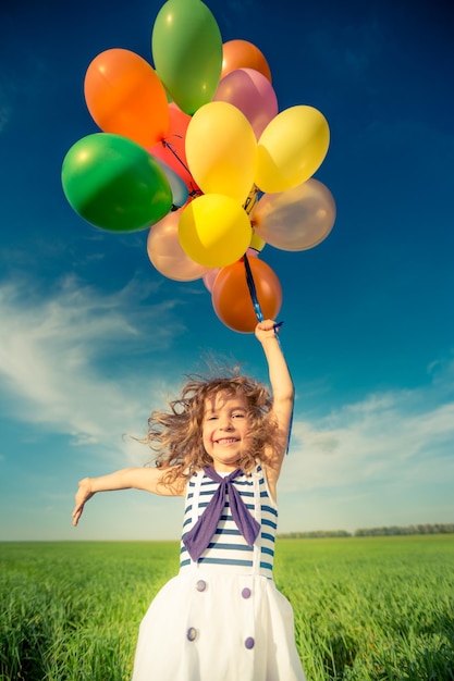 Foto bambino felice che gioca con palloncini colorati giocattolo all'aperto. bambino sorridente che si diverte nel campo verde della primavera su sfondo blu del cielo. concetto di libertà