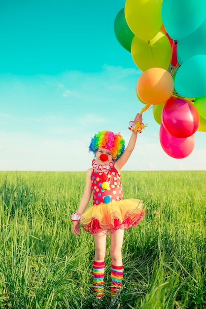 Happy child playing with colorful toy balloons outdoors. Smiling kid having fun in green spring field against blue sky background. Freedom concept