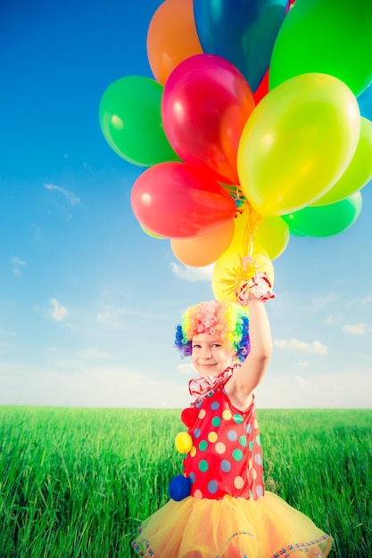 Happy child playing with colorful toy balloons outdoors. Smiling kid having fun in green spring field against blue sky background. Freedom concept