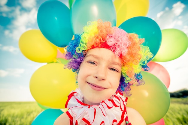 Счастливый ребенок играет с красочными игрушечными воздушными шарами на открытом воздухе. Улыбающийся малыш веселится в зеленом весеннем поле на фоне голубого неба. Концепция свободы