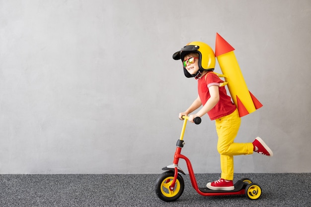 Happy child playing with toy paper rocket against grey concrete wall surface