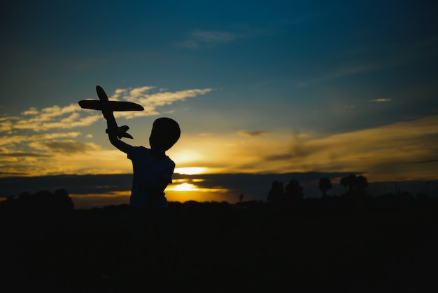 Bambino felice che gioca con un aereo giocattolo in natura durante il tramonto estivo