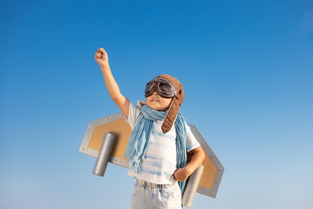 Happy child playing with toy wings against blue sky background.\
kid having fun outdoor in summer. imagination and children dream\
concept