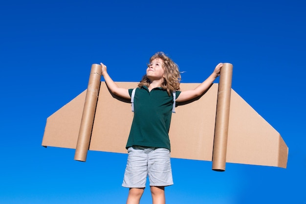 Happy child playing with toy wings against summer sky background kids success leader and winner concept