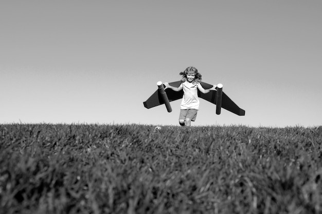 Happy child playing with toy wings against summer sky and green grass background kids success leader