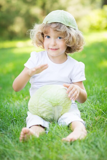 Happy child playing with vegetables on green grass in spring park Healthy eating concept