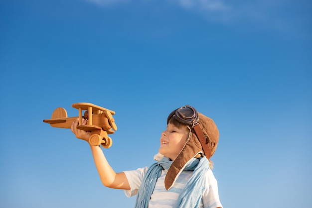 Happy child playing with vintage wooden airplane. Kid having fun outdoor in summer. Imagination and freedom concept