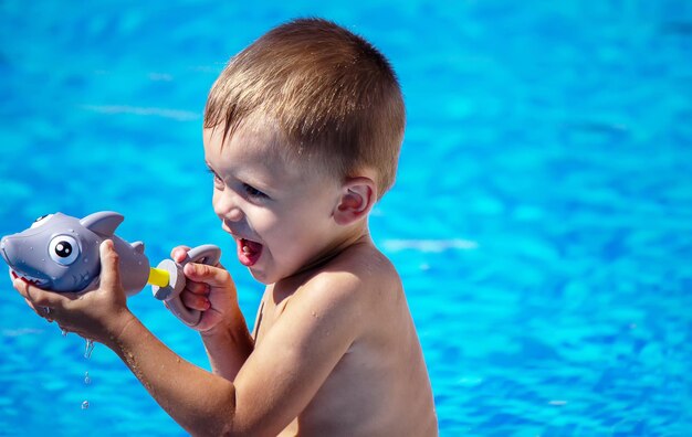 Happy child in the pool playing with a water gun.