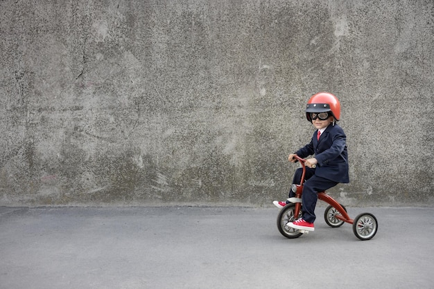 Happy child pretend to be businessman. Funny kid riding bike outdoor. Back to work, start up and business idea concept