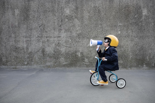 Happy child pretend to be businessman. Funny kid riding bike outdoor. Boy shouting through loudspeaker. Back to work, start up and business idea concept