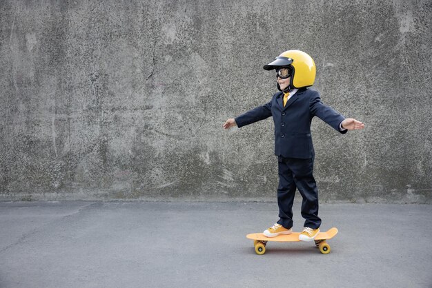 Happy child pretend to be businessman. Funny kid riding skateboard outdoor. Back to work, start up and business idea concept