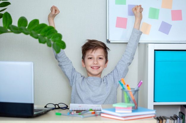 幸せな子供は手を挙げて、自宅のコンピューターで宿題をしました。ホーム遠隔オンライン教育。