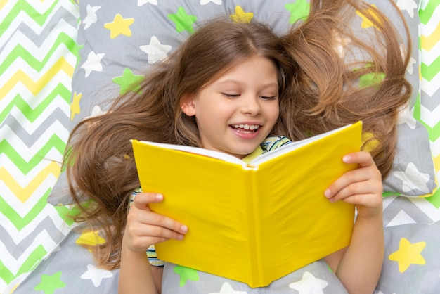 A happy child reads a book in bed before going to bed.