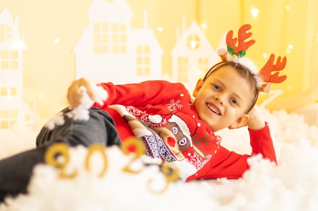 A happy child in a red knitted sweater with with santa's reindeer on the background of numbers 2023