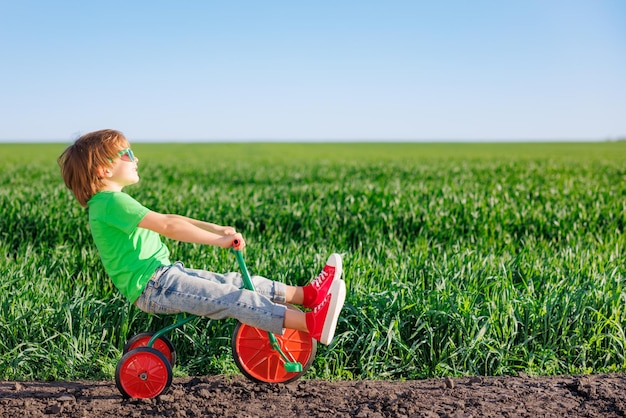 Happy child riding bike outdoor in spring green field