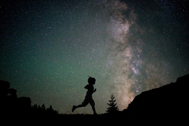 Siluetta corrente corrente del bambino felice con la via lattea e bello cielo notturno in pieno delle stelle nella priorità bassa