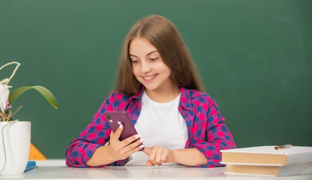 Happy child at school chatting on phone on blackboard background communication