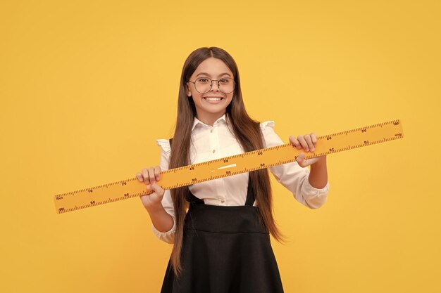 Happy child in school uniform and glasses hold mathematics ruler for measuring geometry