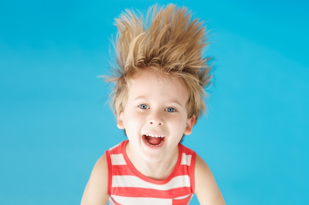 Happy child shouting against blue paper background Funny kid hanging upside down Summer vacation and travel concept