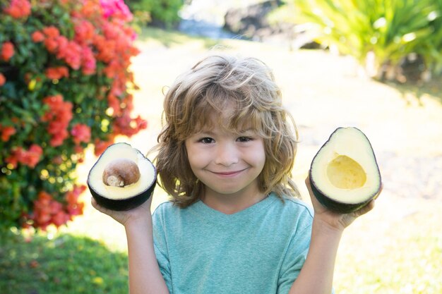 Happy child showing avocado on summer garden kids healthy food