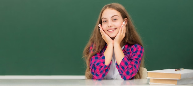 Happy child sit at school on blackboard background knowledge day Banner of schoolgirl student School child pupil portrait with copy space