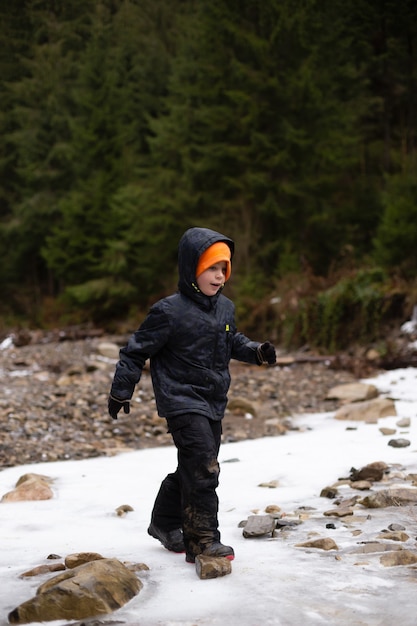 Happy child in sportswear walks through a frozen mountain river