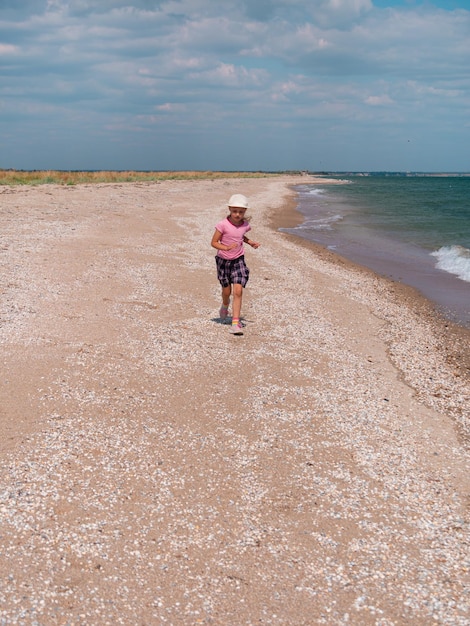 Photo happy child in straw hat running jumping having fun on empty autumn beach blond girl walking on sand