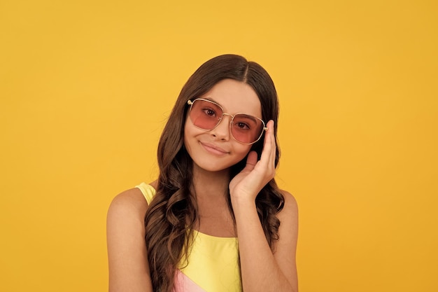 Happy child in summer glasses has curly hair on yellow background beauty