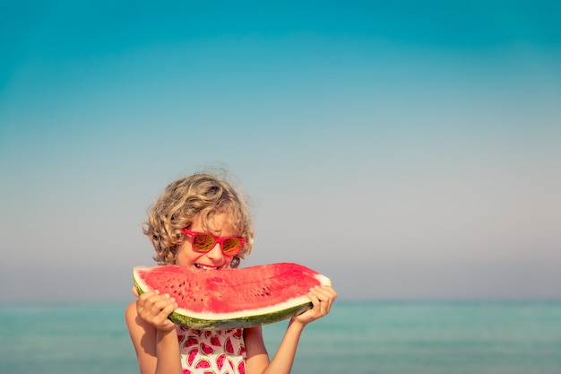 Happy child on summer vacation Kid eating watermelon on the beach Healthy food concept