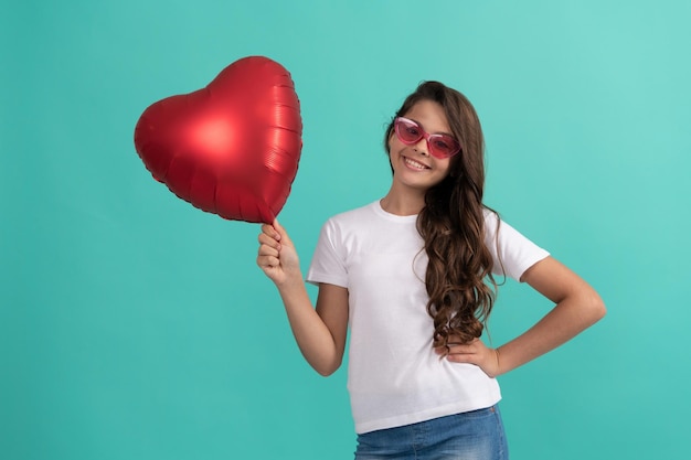 Il bambino felice in occhiali da sole tiene il palloncino del partito del cuore rosso per il simbolo dell'amore di san valentino, la vendita di san valentino.