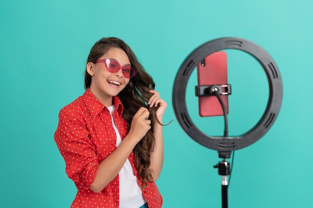 Happy child in sunglasses showing her long hair blogging online with selfie led, blogger