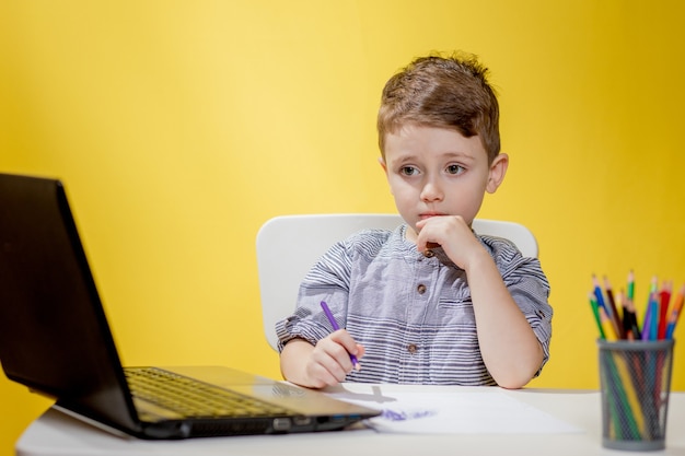 Счастливый ребенок с помощью цифрового ноутбука делает домашнее задание на желтом фоне