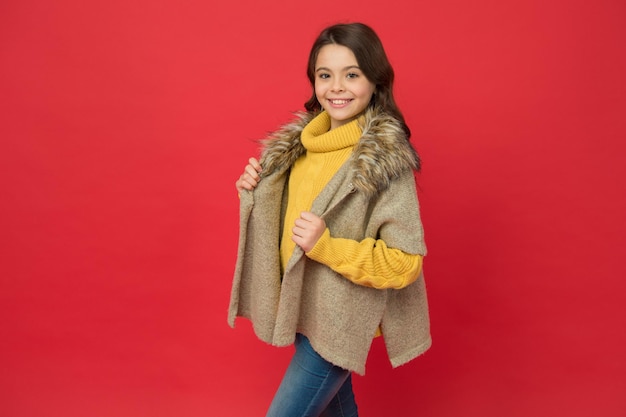 Happy child wear knitted sweater and waistcoat teen girl has long curly hair happy childhood trendy child on red background warm clothes and knitwear kid autumn fashion style Excitement