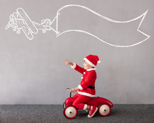 Foto bambino felice che indossa il costume di natale kid riding auto giocattolo vacanze di natale concept