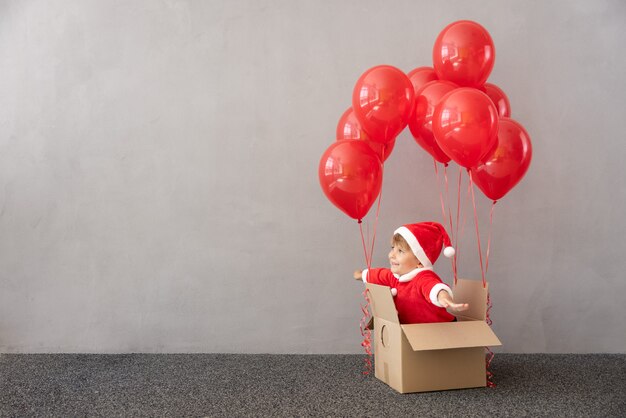 Happy child wearing Christmas costume Kid sitting in box with red balloons