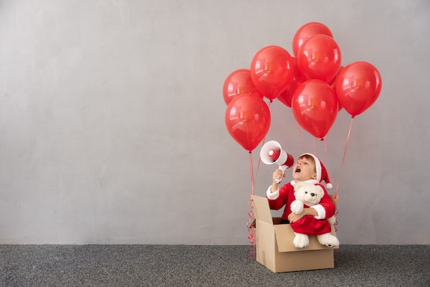 Bambino felice che indossa il costume di natale bambino seduto in una scatola con palloncini rossi