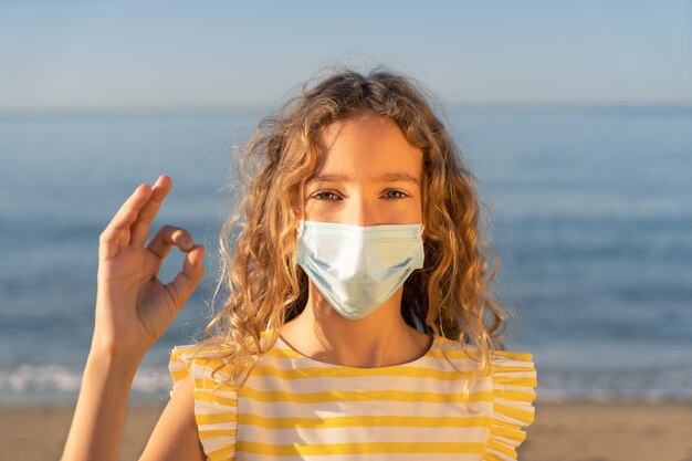 Happy child wearing medical mask outdoor against blue sky.