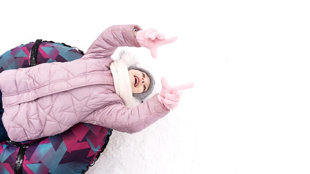 A happy child in winter clothes lies on a colored sled and laughs