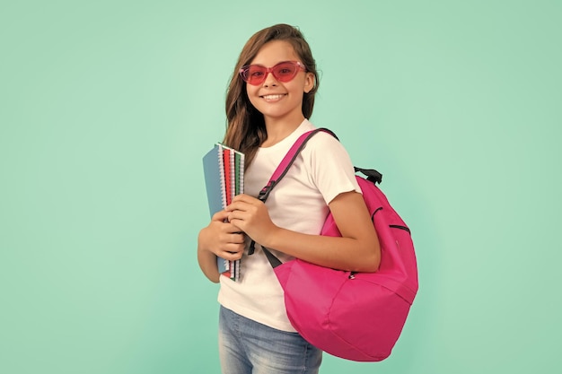 Счастливый ребенок с рюкзаком и тетрадью в солнцезащитных очках готов учиться в школе