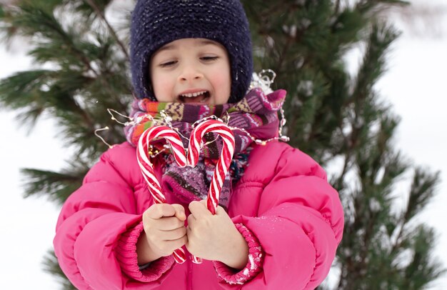 Bambino felice con un grande bastoncini di zucchero sotto un albero di natale. concetto di vacanze invernali.